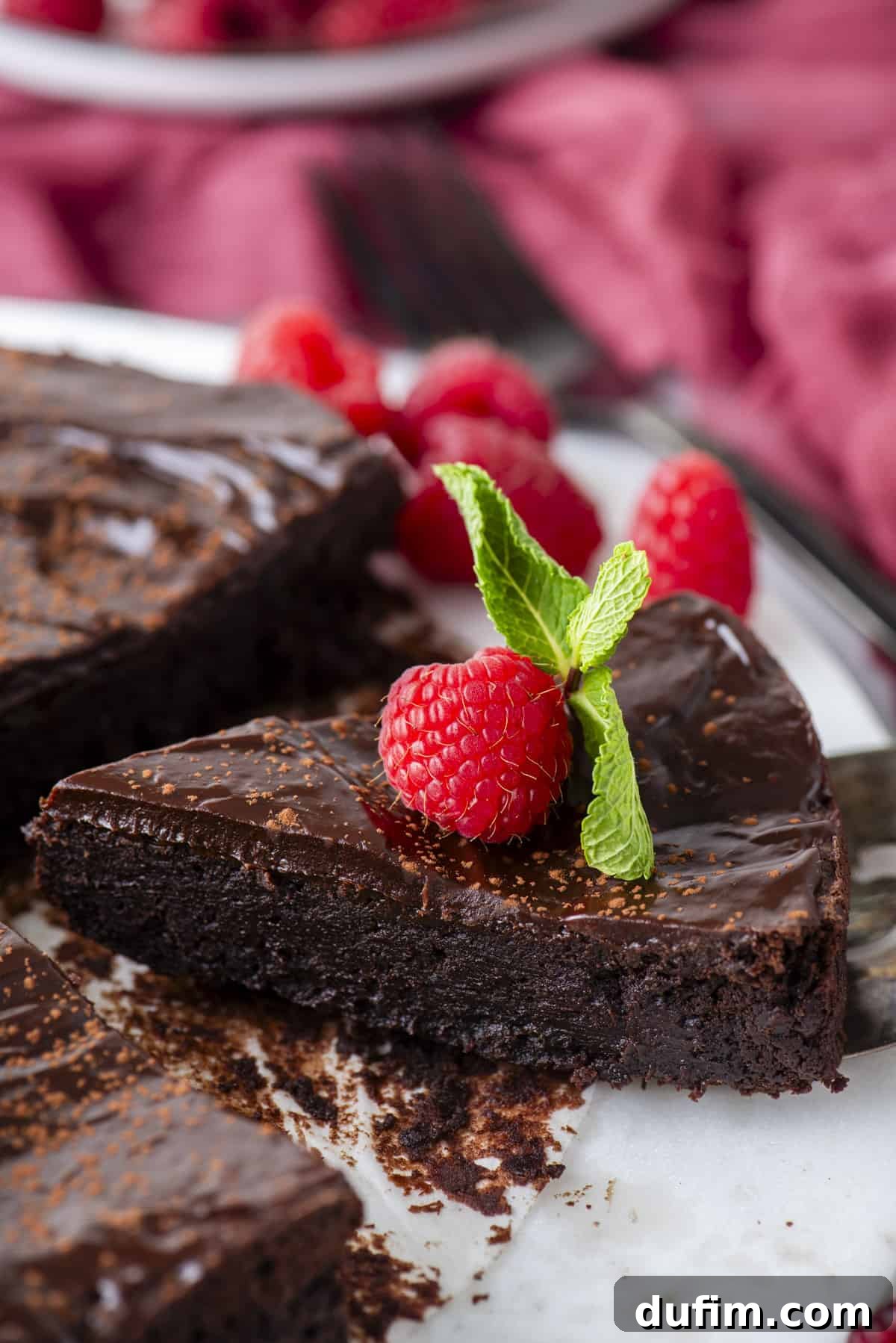 Decadent Flourless Chocolate Cake 19 a slice of flourless chocolate cake being lifted away from the rest of the cake, topped with a fresh raspberry and mint leaves