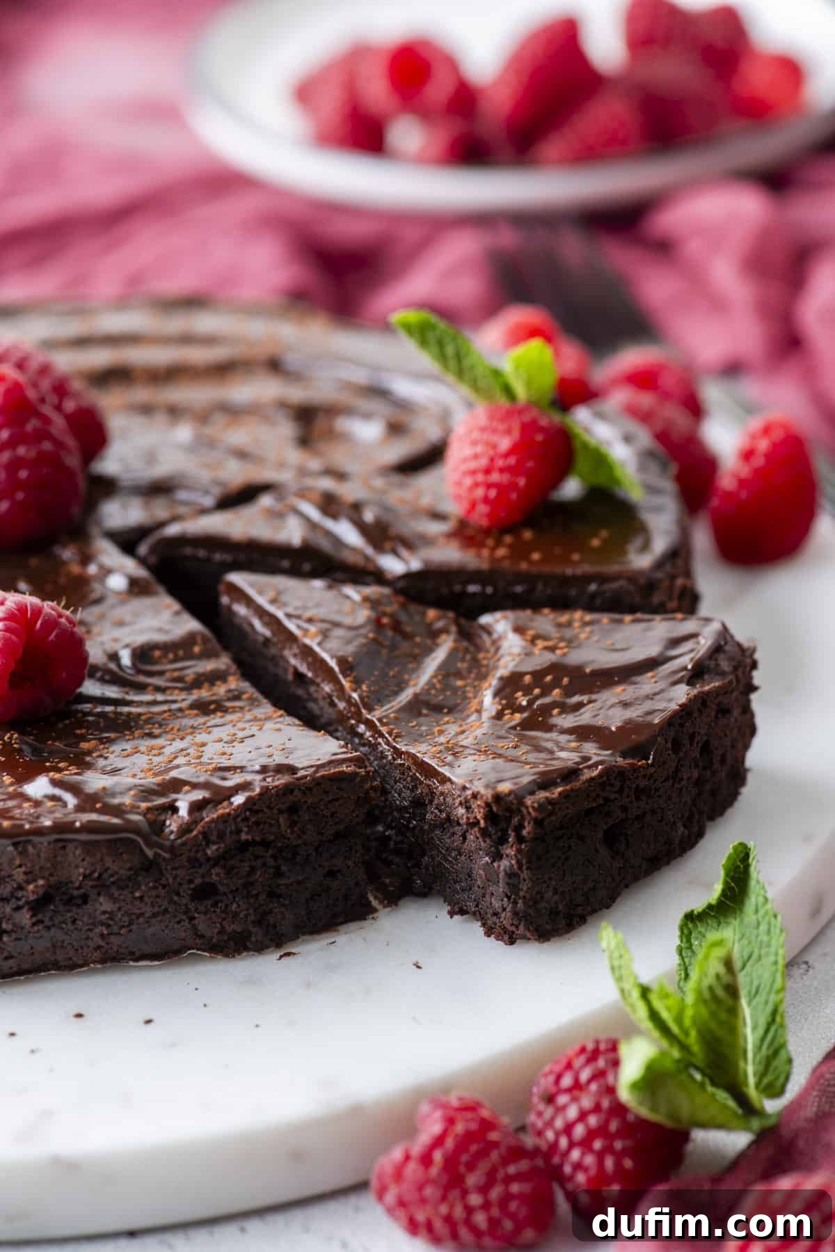 Decadent Flourless Chocolate Cake 3 flourless chocolate cake on a round white serving platter with one slice of cake cut, topped with fresh raspberries and mint leaves