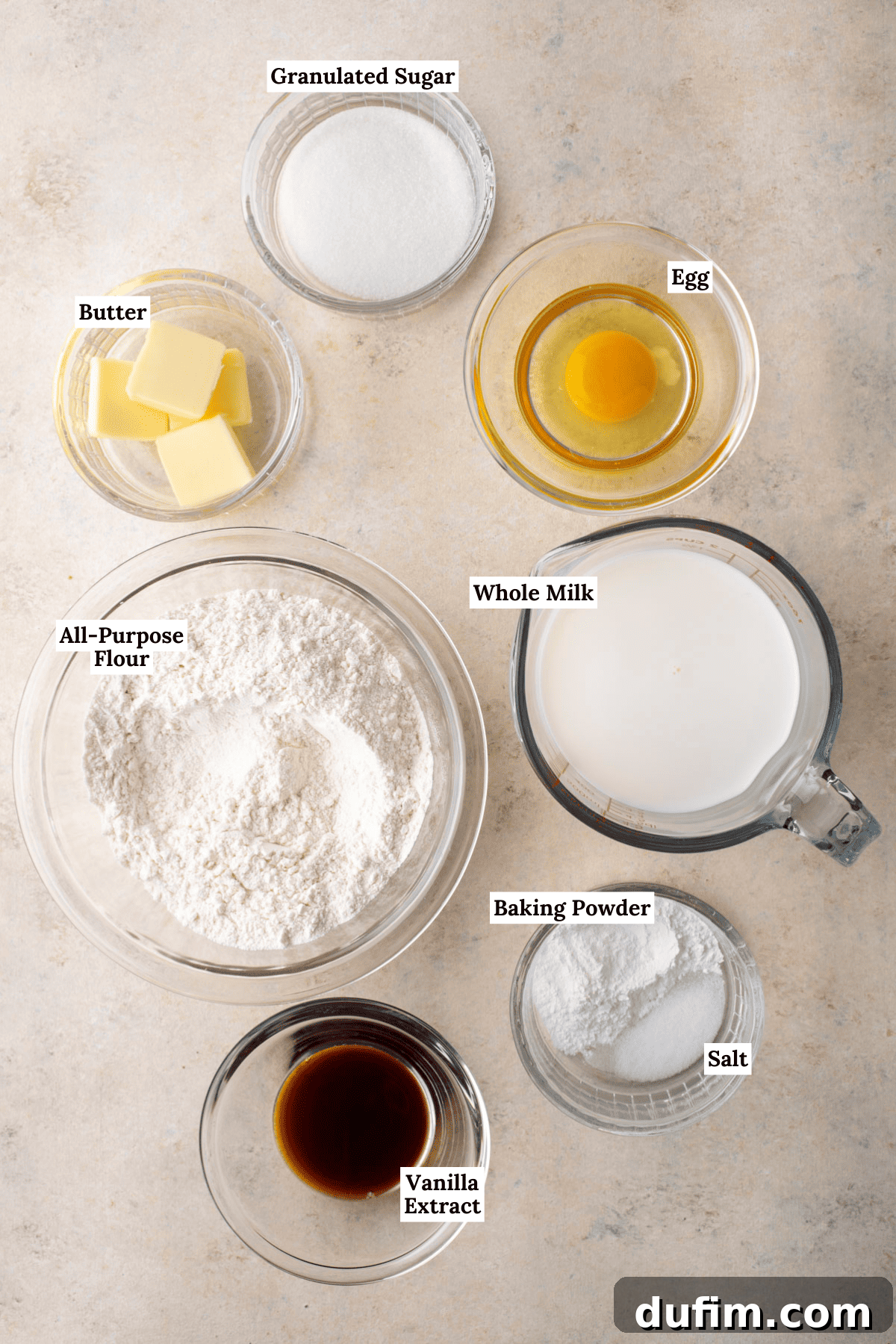 A visually appealing flat lay of essential pancake ingredients: all-purpose flour, granulated sugar, baking powder, and salt in their dry form, alongside a jug of milk, a single egg, a stick of unsalted butter, and a bottle of vanilla extract. These simple components are the building blocks of perfectly fluffy pancakes.