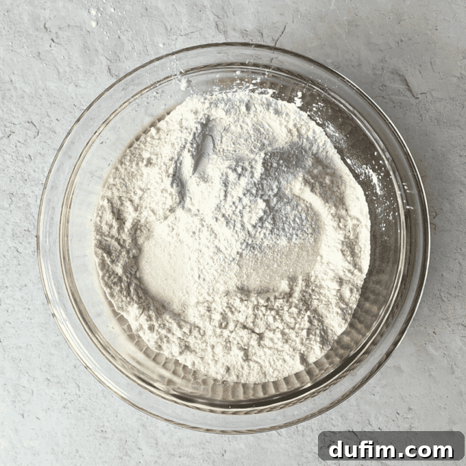 A clear glass mixing bowl contains the precise dry ingredients for homemade pancakes: all-purpose flour, granulated sugar, baking powder, and salt, perfectly measured and ready for whisking.