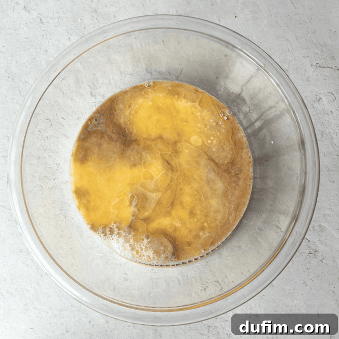 A separate clear glass bowl holds the wet ingredients for fluffy pancakes: milk, melted and cooled unsalted butter, a fresh egg, and aromatic vanilla extract, all ready to be whisked together.