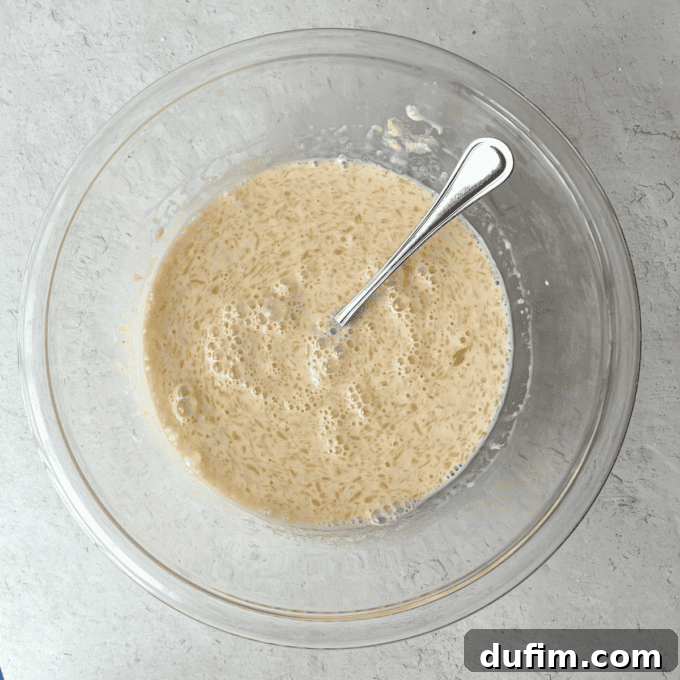 A close-up shot of the whisked wet ingredients—milk, melted butter, egg, and vanilla extract—in a clear glass bowl, showcasing their smooth, combined texture, ready for the next step in pancake preparation.
