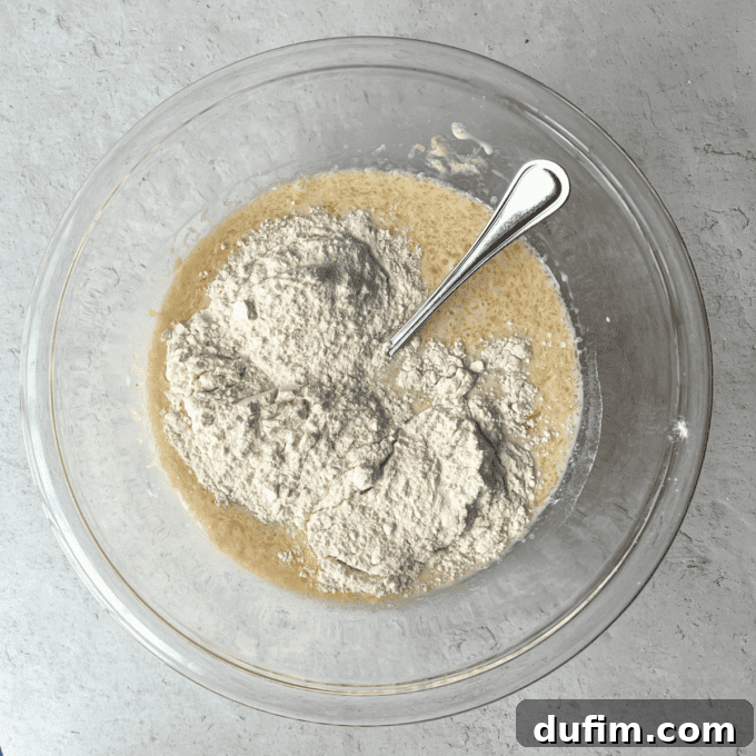 The wet ingredients are gently poured into the bowl of dry ingredients for pancakes, demonstrating the careful combination process before whisking lightly to form the batter.