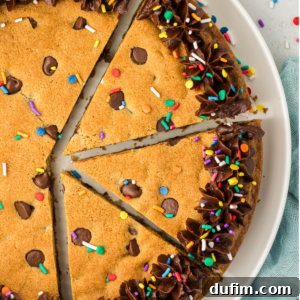 A sliced round cookie cake decorated with chocolate frosting and colored sprinkles on a white plate, showcasing its festive appeal.