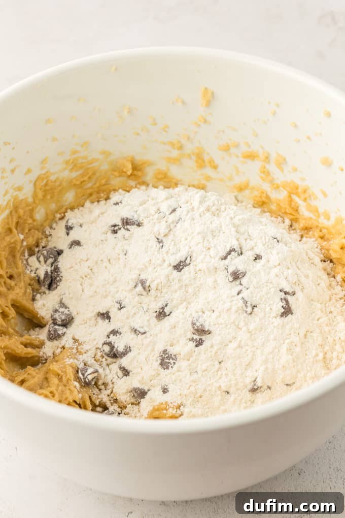 The combined wet and dry ingredients for the cookie cake in a white bowl, not yet fully mixed, illustrating the initial stage of combining the dough.