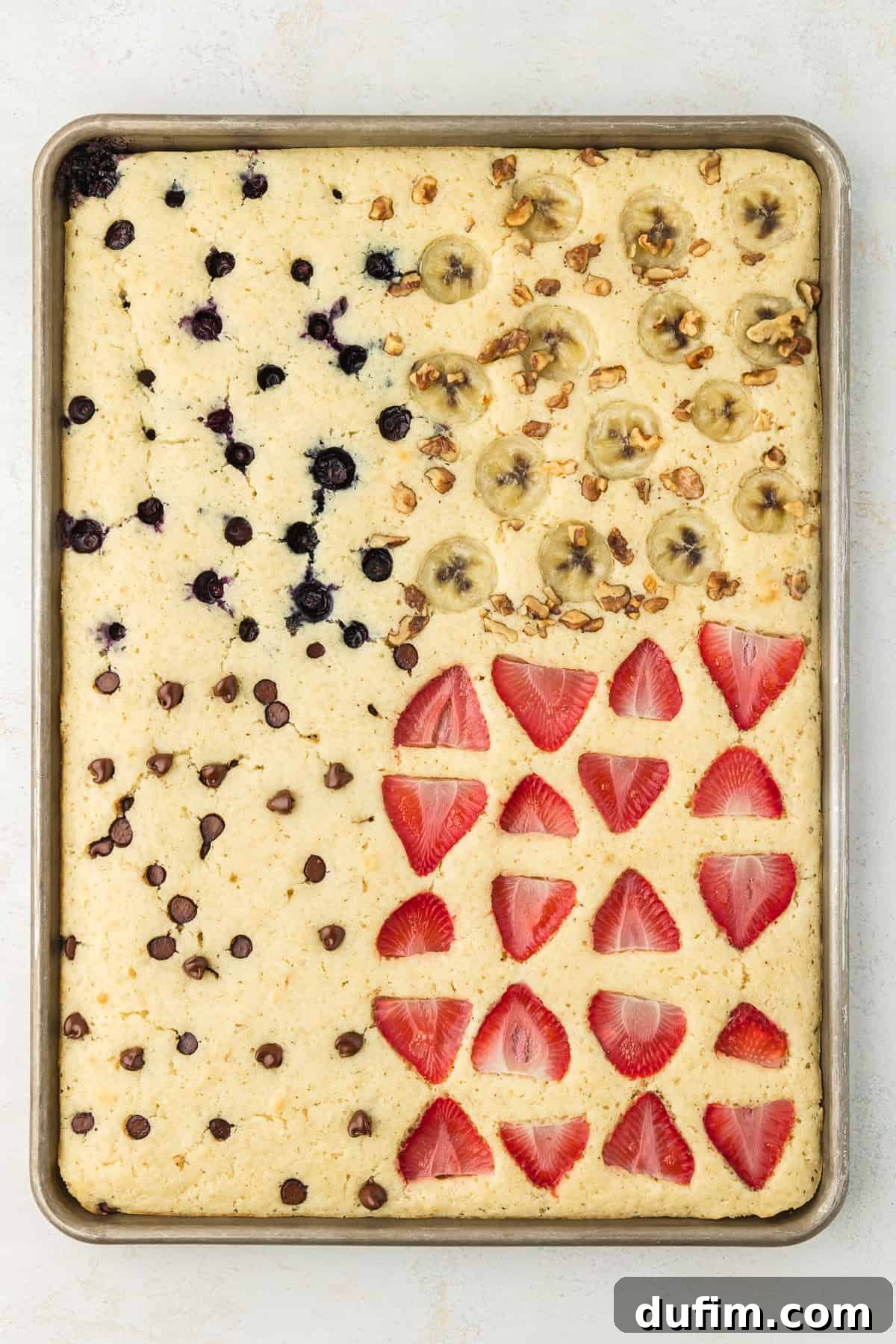 A sheet pan full of pancakes, blueberry pancakes in the upper left corner, banana walnut pancakes in the upper right corner, chocolate chip pancakes in the lower left corner and strawberry pancakes in the lower right corner