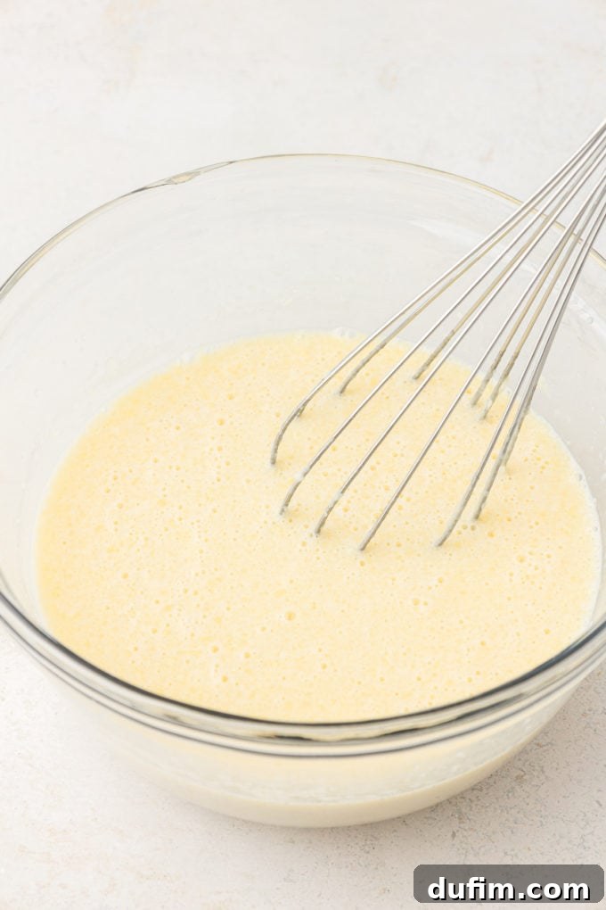 wet ingredients for sheet pan pancakes in a clear glass bowl with a whisk leaning inside the bowl