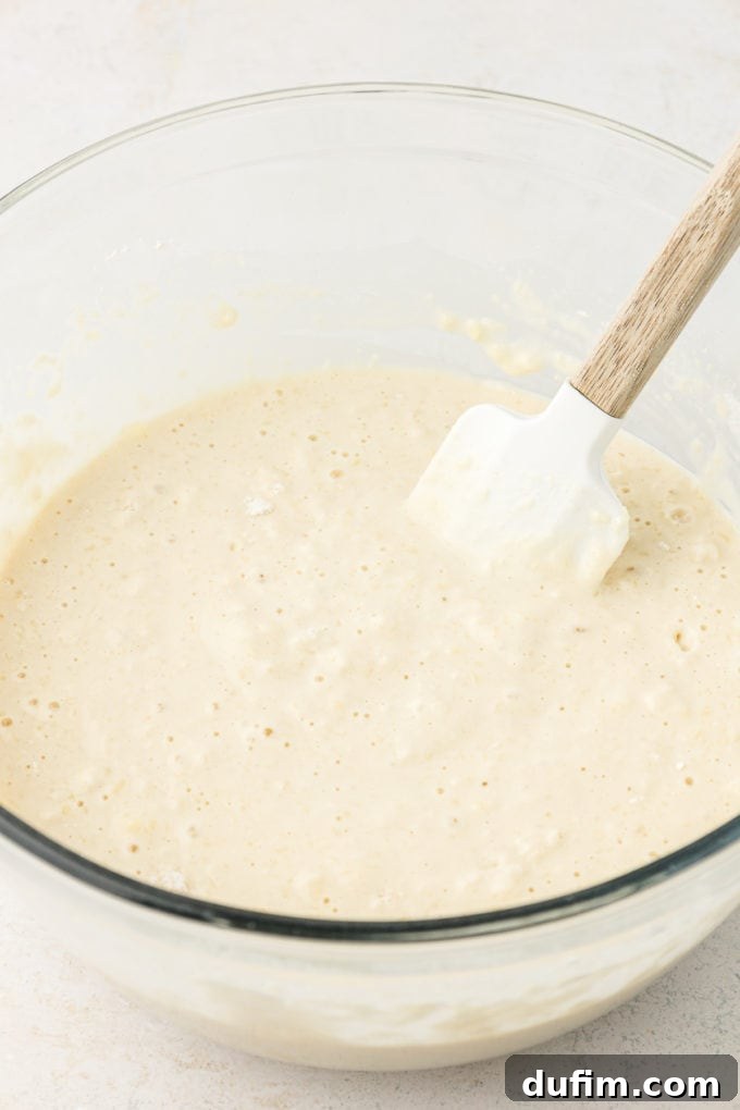 sheet pan pancake batter in a clear glass bowl on a white surface with a spatula leaning inside the bowl