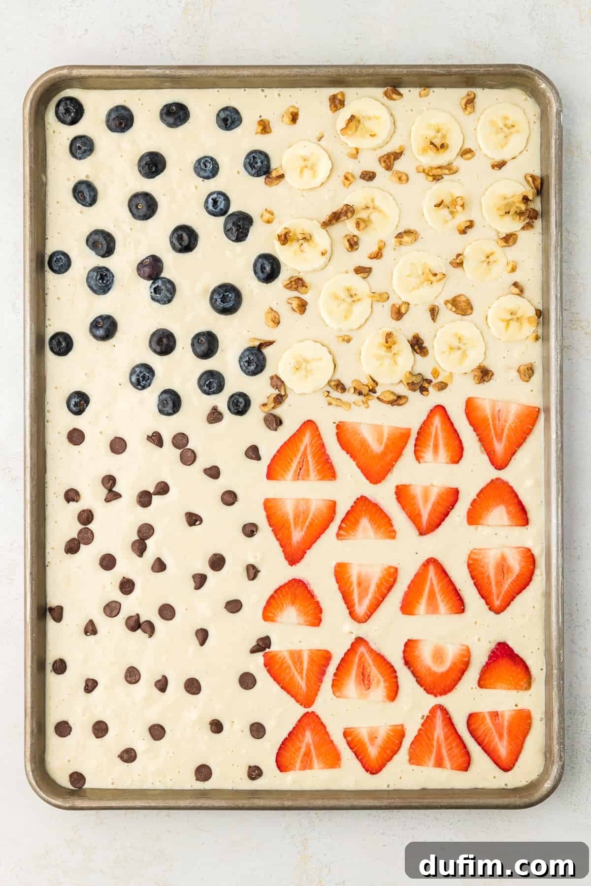 A sheet pan full of pancake batter, blueberry pancakes in the upper left corner, banana walnut pancakes in the upper right corner, chocolate chip pancakes in the lower left corner and strawberry pancakes in the lower right corner