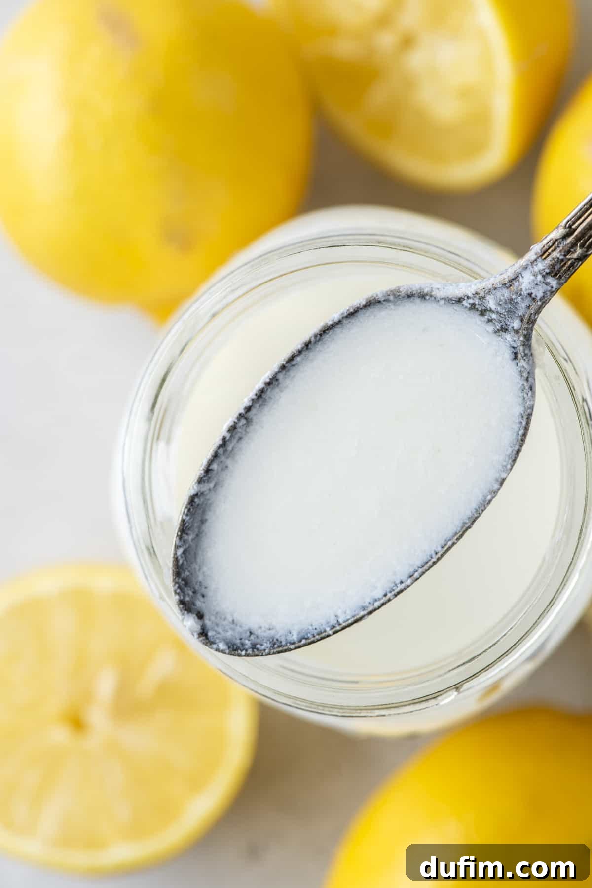 A spoon full of buttermilk being held above a mason jar full of buttermilk with fresh whole and sliced lemons all around