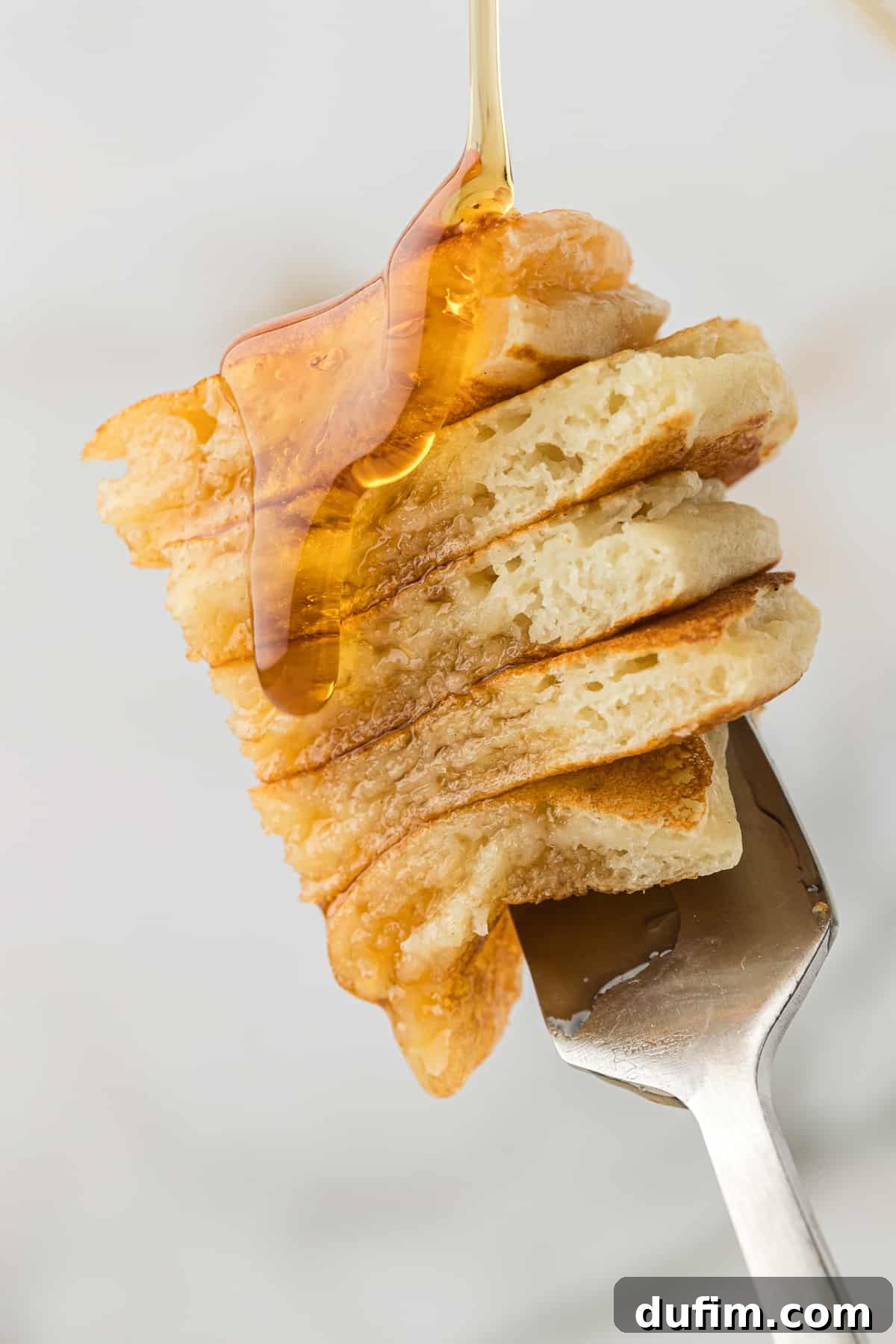 Simple Secrets to Fluffy Buttermilk Pancakes 4 A fork holding five small, perfectly cut slices of fluffy buttermilk pancake, each piece gently coated with a thin, glistening layer of maple syrup. The image highlights the inviting texture and delicious appeal of the pancakes.