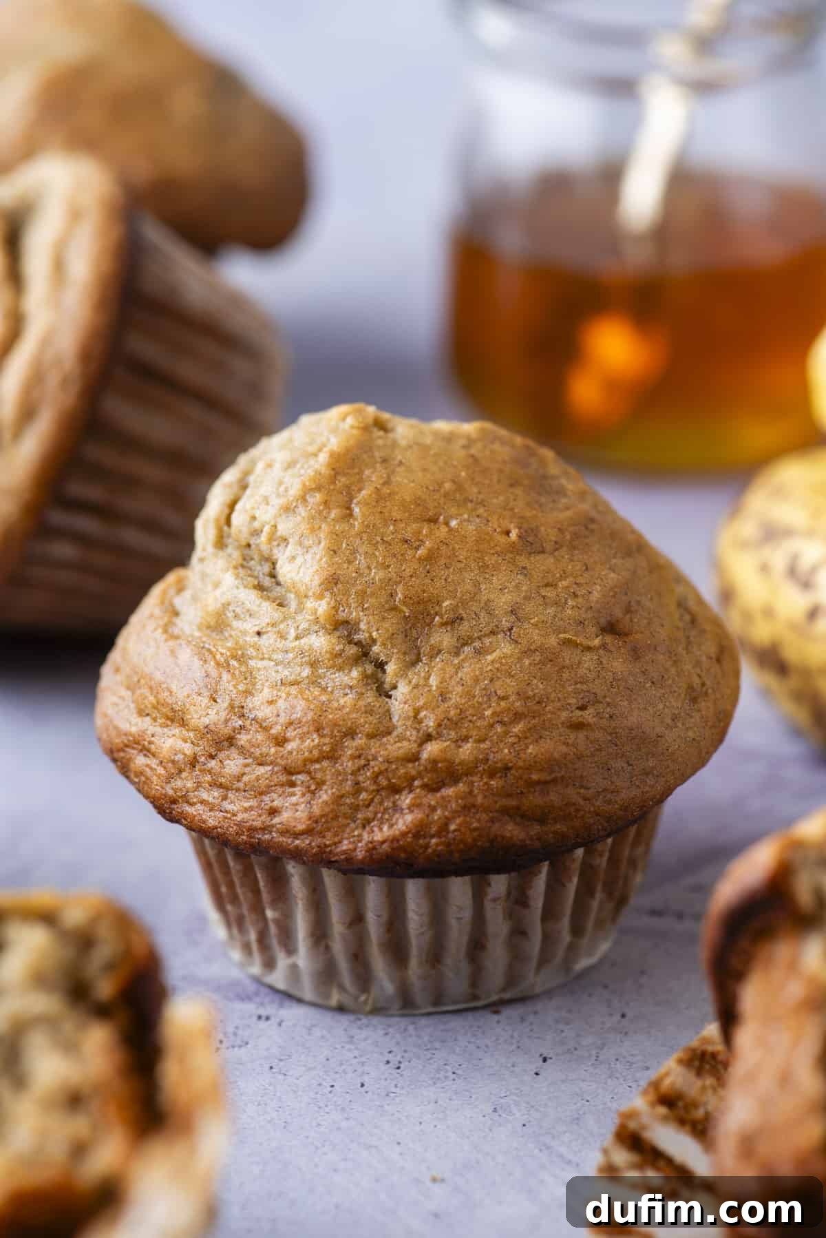 Healthy banana muffins on a purple background with a jar of honey and fresh bananas in the background, highlighting natural ingredients.