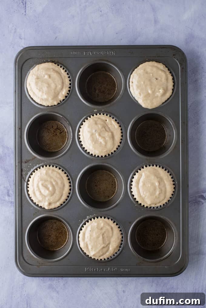 Muffin pan filled with healthy banana muffin batter, strategically leaving empty wells for optimal doming.