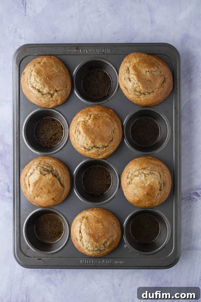 Freshly baked healthy banana muffins with golden, domed tops cooling in a muffin pan.
