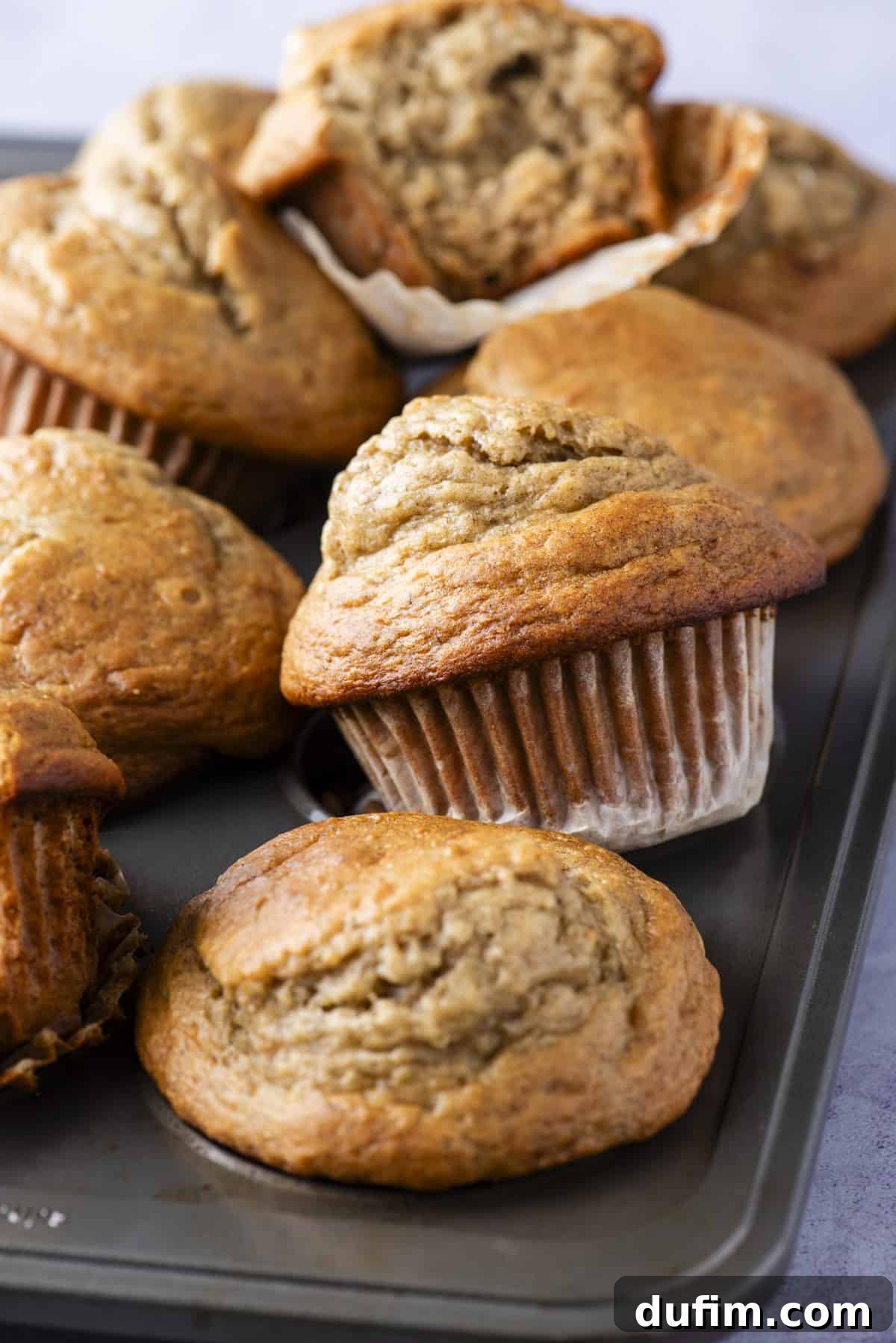 Healthy banana muffins cooling in a metal muffin pan, showcasing their golden, domed tops and perfect individual shapes.