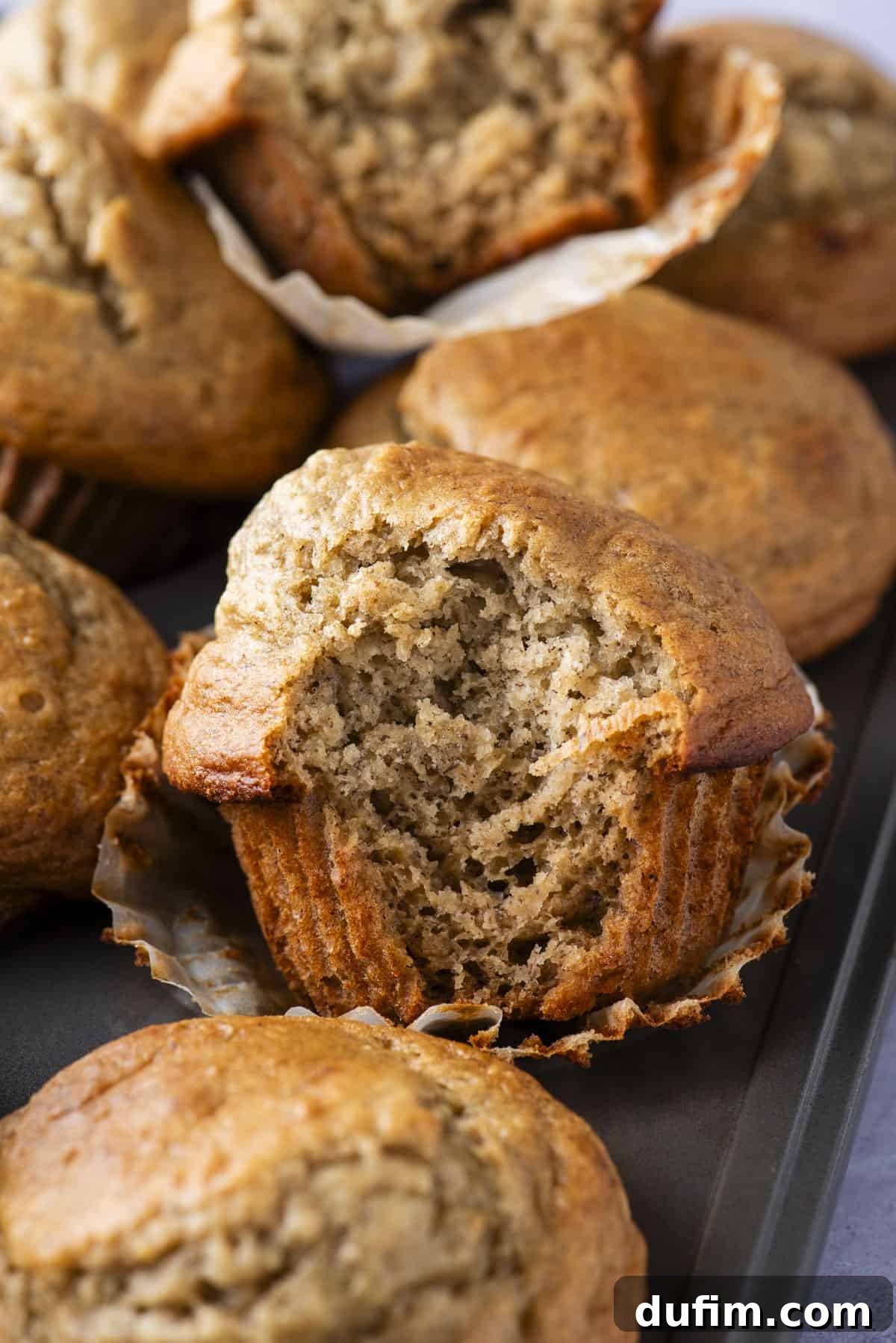 Healthy banana muffins arranged in a muffin pan, with one muffin having a bite removed to showcase its moist interior.