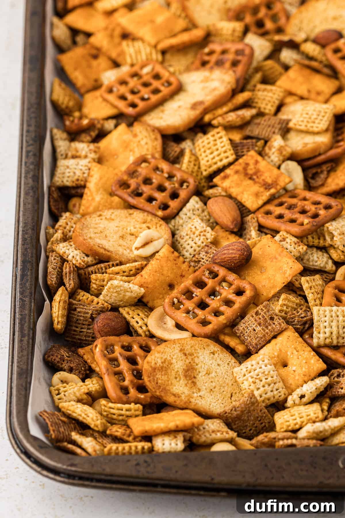 Unlock the Secret to Perfect Chex Mix 13 A partial, close-up view of a baking sheet completely full of golden, seasoned homemade Chex Mix, highlighting the texture and even coating.