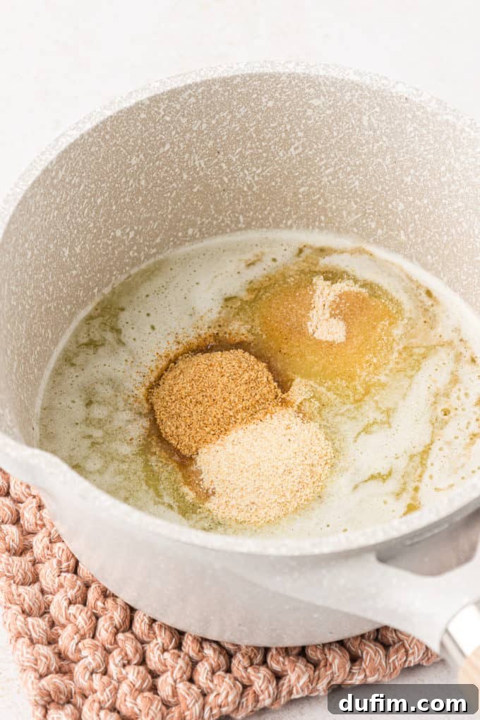 Unlock the Secret to Perfect Chex Mix 6 A small pot sitting on a knit pot holder with butter and the dry seasonings (Worcestershire, seasoned salt, garlic powder, onion powder) not yet mixed, showcasing the separate components.