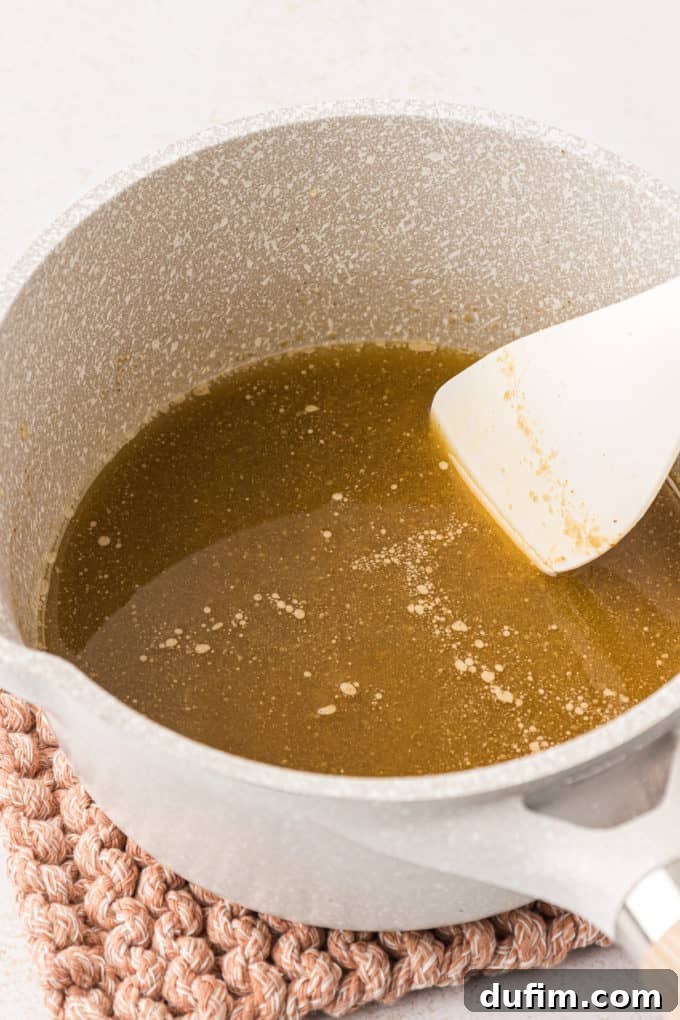 Unlock the Secret to Perfect Chex Mix 7 A small pot on a knit pot holder with the seasoned butter mixture being stirred by a white spatula, showing the rich, combined sauce.