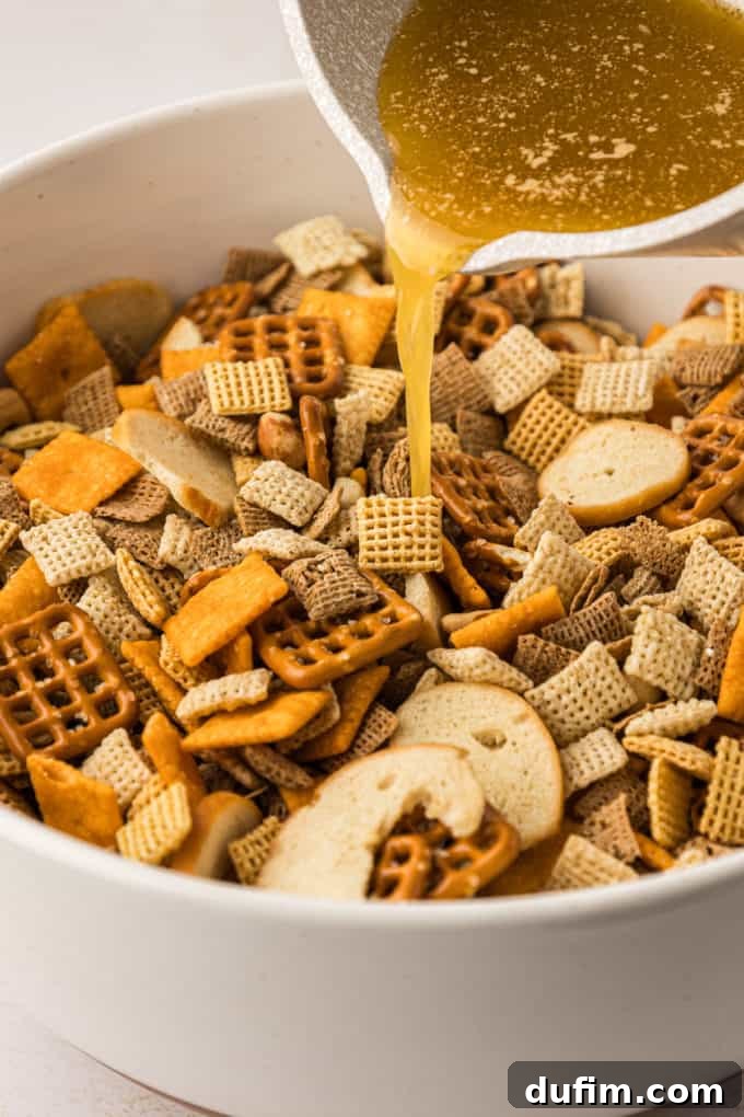 Unlock the Secret to Perfect Chex Mix 8 A white bowl full of Chex Mix ingredients with the seasoned butter mixture being poured over, illustrating the next step in the preparation.