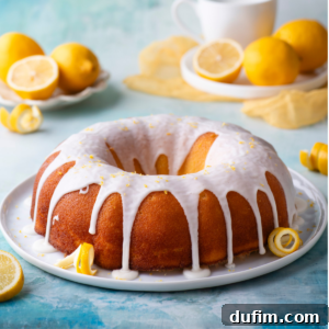 A glistening lemon bundt cake on a round, white plate, surrounded by fresh lemon peels, sitting on a charming blue surface with additional fresh lemons and slices arranged around it.