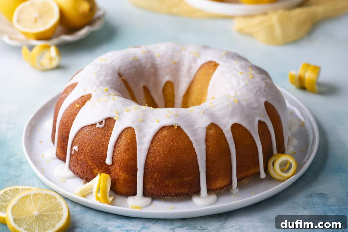 A whole lemon bundt cake beautifully presented on a round, white plate, surrounded by vibrant fresh lemon peels and slices, set on a serene blue surface. Small white plates holding additional lemons complete the inviting scene.