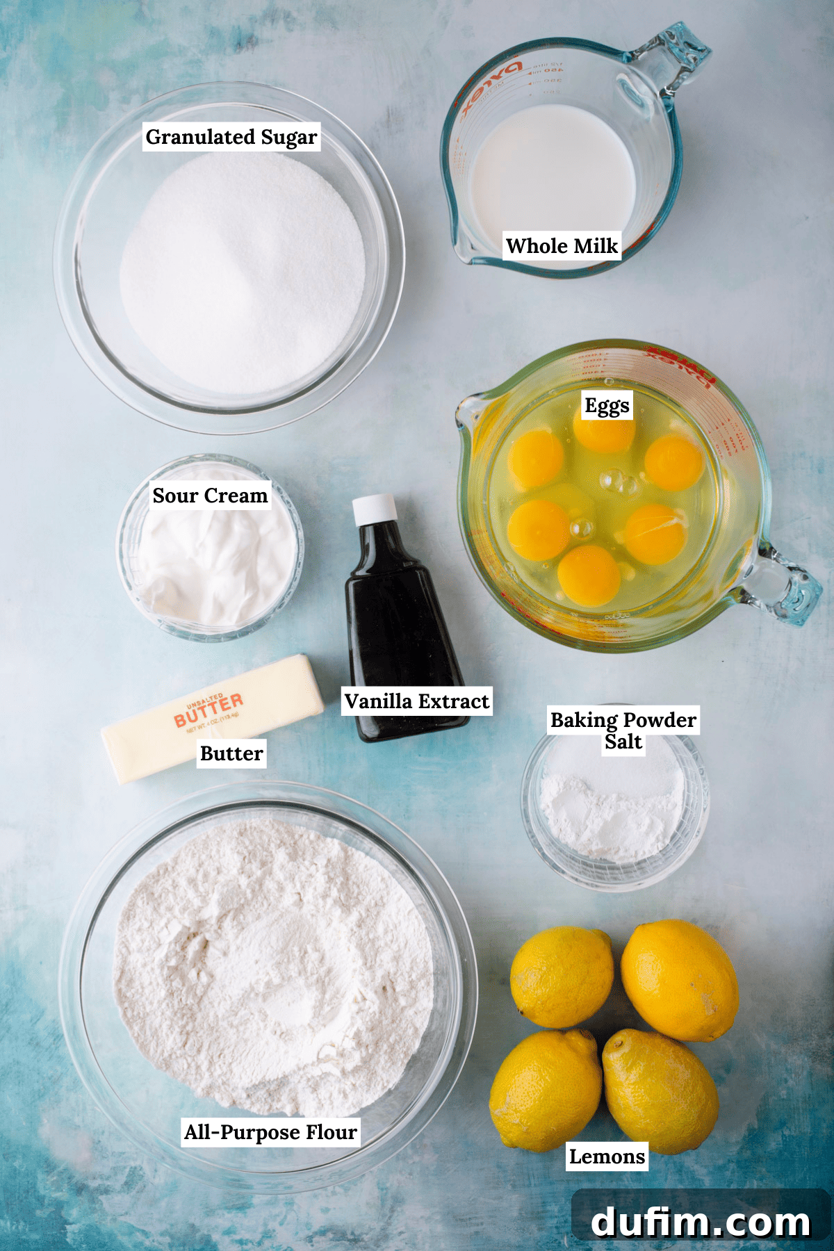 An overhead view showcasing all the essential ingredients for a lemon bundt cake, meticulously arranged on a clean surface. These include granulated sugar, creamy whole milk, tangy sour cream, fresh eggs, aromatic vanilla extract, softened butter, baking powder, a pinch of salt, all-purpose flour, and bright, zesty fresh lemons.