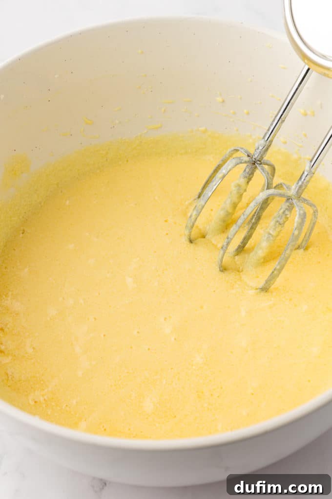 wet ingredients for vanilla bundt cake in a white bowl with the whisks of an electric mixer leaning inside the bowl