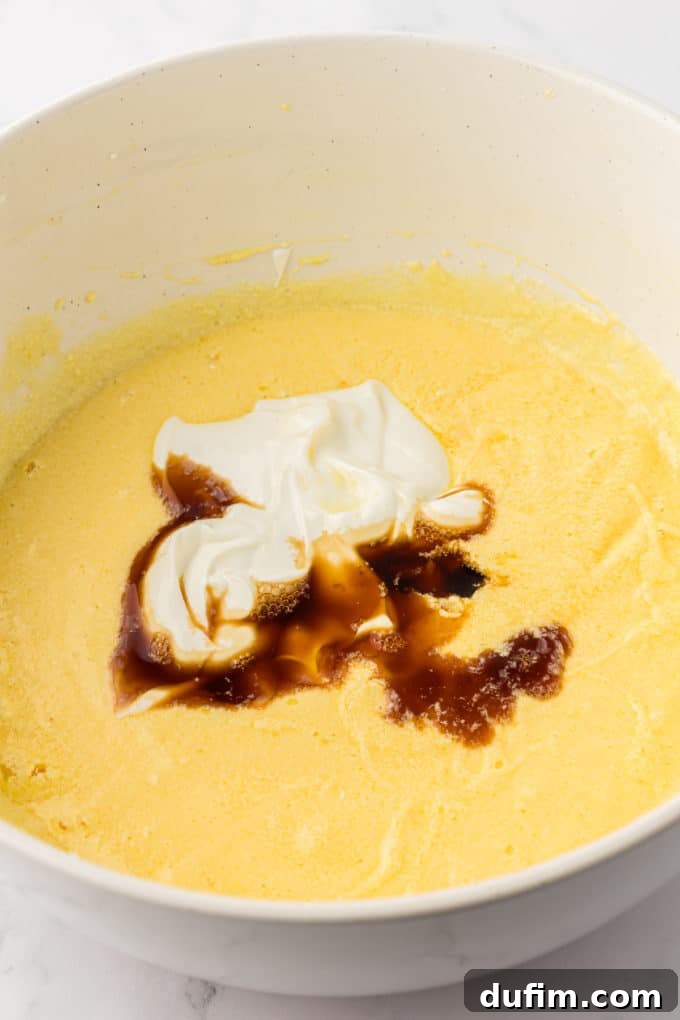 wet ingredients for vanilla bundt cake in a white bowl with sour cream and vanilla extract on top that have not been mixed in yet