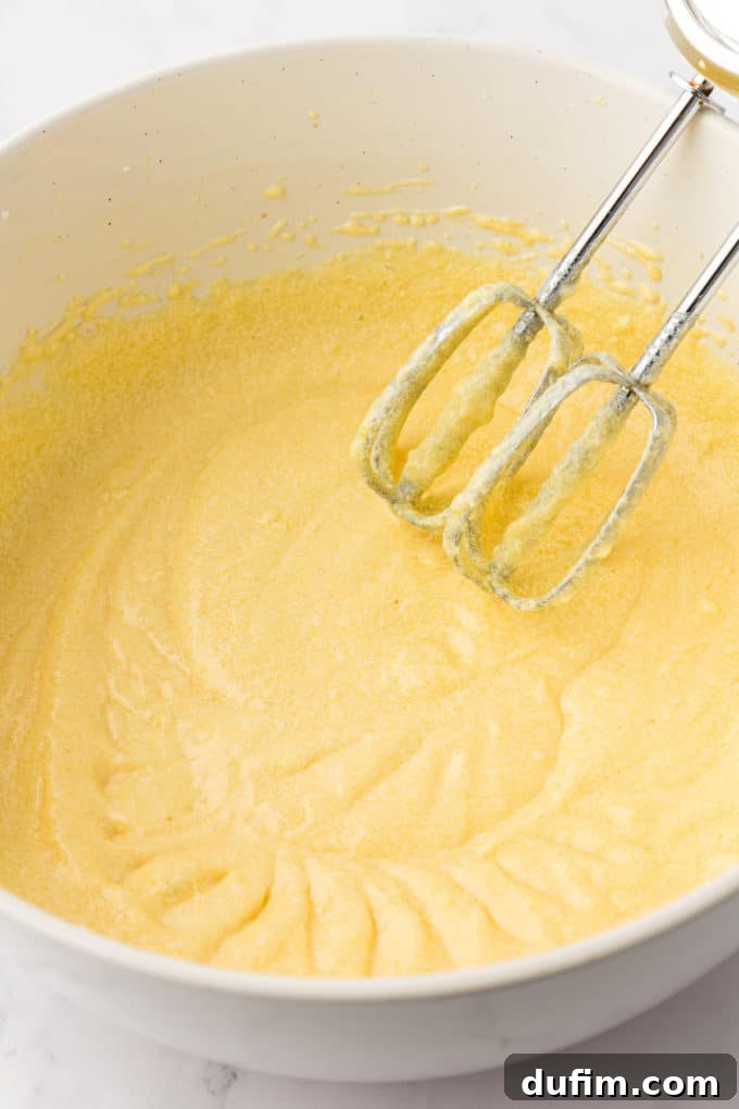 wet ingredients for vanilla bundt cake in a white bowl with the whisks of an electric mixer leaning inside the bowl