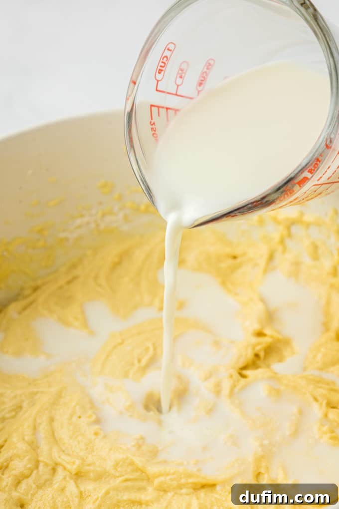 batter for vanilla bundt cake in a white bowl with a measuring cup of milk being poured on top