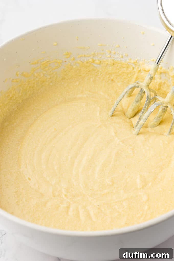 batter for vanilla bundt cake in a white bowl with the whisks of an electric mixer leaning inside the bowl