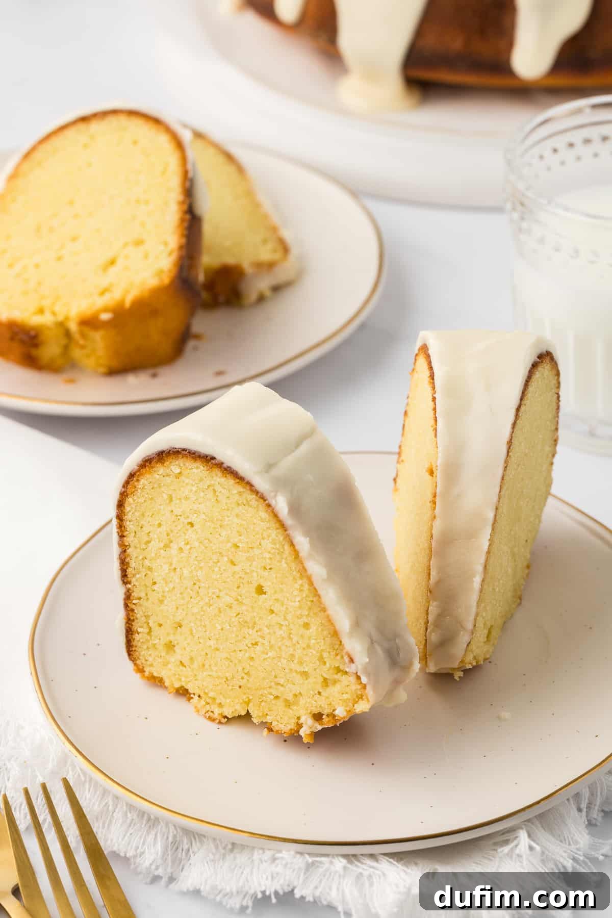 two slices of vanilla bundt cake on a small white plate with a fork beside it, another plate with slices behind it, and a small glass of milk