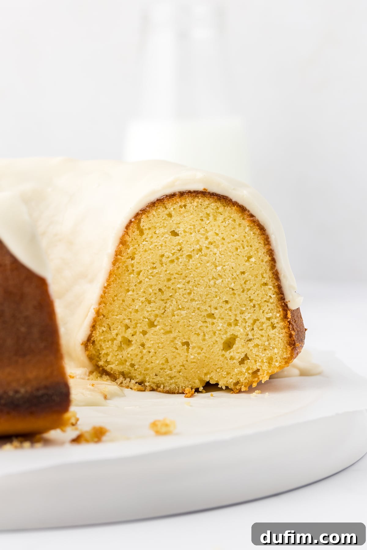 side view of a vanilla bundt cake with slices missing, exposing the inside of the cake with the glaze layer on top