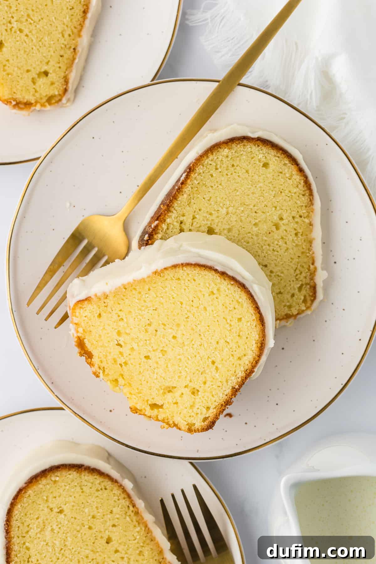 overhead view of two slices of vanilla bundt cake on a small white plate with a fork, with two more plates with a slice of cake beside it