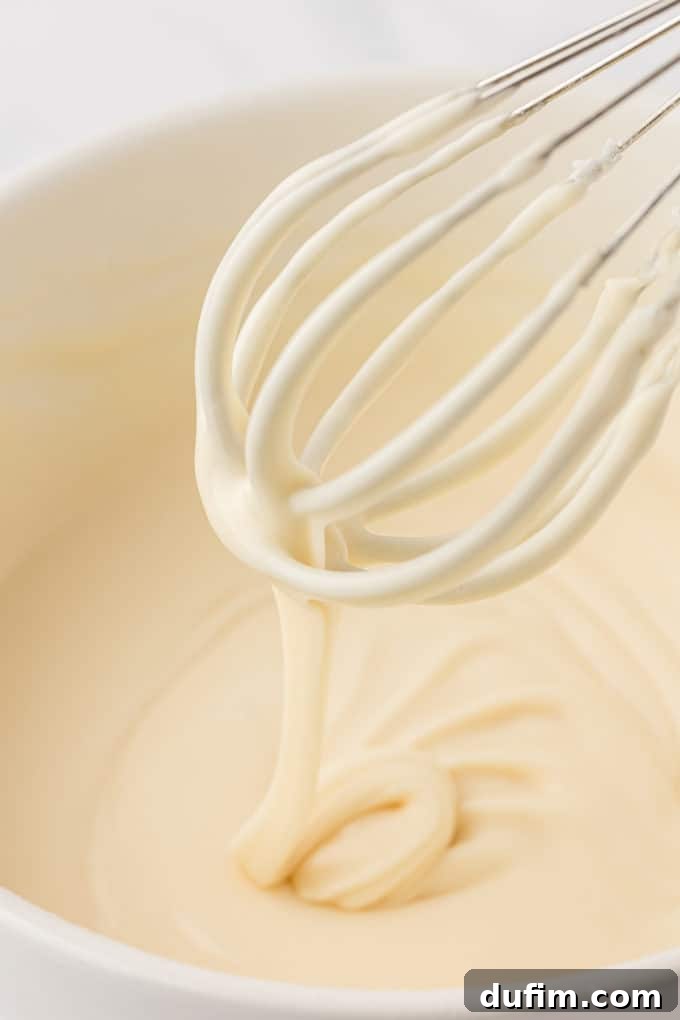 vanilla glaze being drizzled off a wire whisk into a white bowl full of glaze
