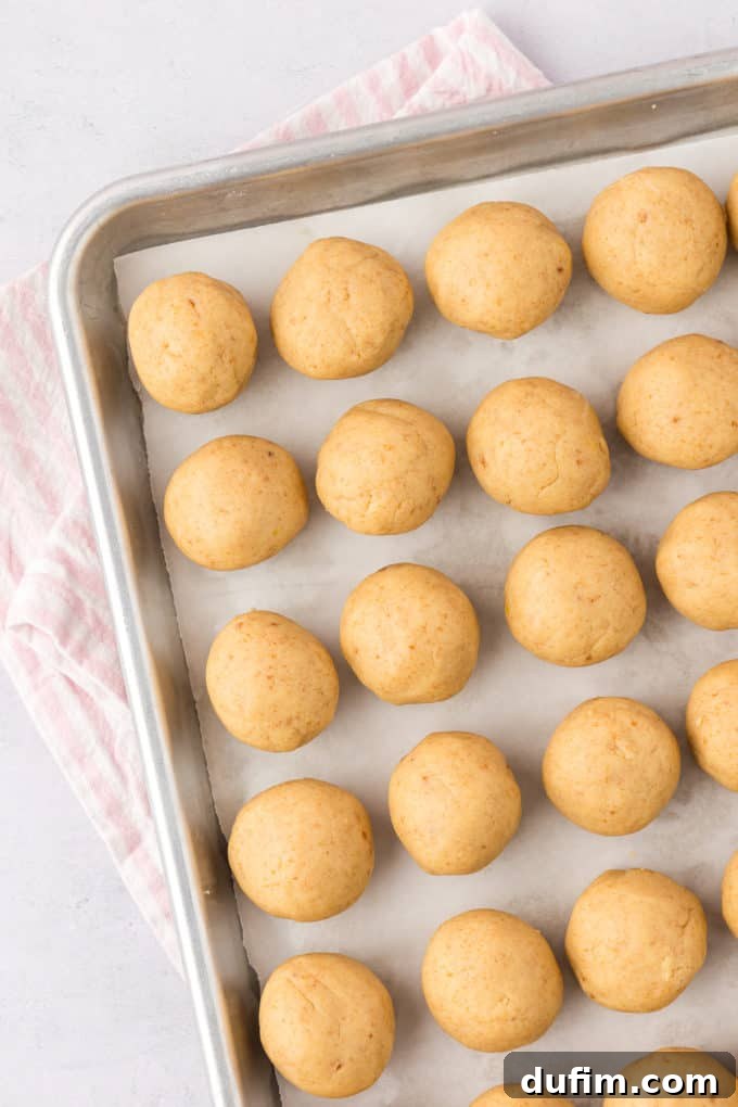 A pristine baking sheet, neatly lined with rows of uniformly sized cake pop balls, rests gently on a stylish white and pink striped towel. The cake balls are firm and smooth, perfectly prepared for their essential chilling period in the refrigerator.