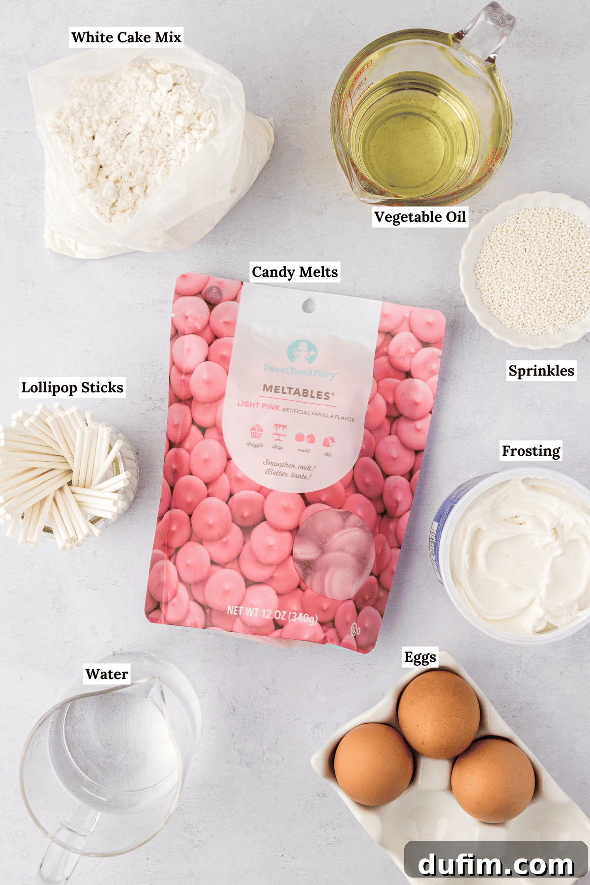 An inviting overhead view of all the essential cake pop ingredients arranged on a surface. Visible items include a bag of white cake mix, a clear glass measuring cup filled with vegetable oil, a cluster of lollipop sticks, a bag of vibrant pink candy melts, a white bowl brimming with white sprinkles, a can of creamy white frosting, a clear cup of water, and three fresh eggs. This photo showcases the simple, accessible components needed to create delicious homemade cake pops.