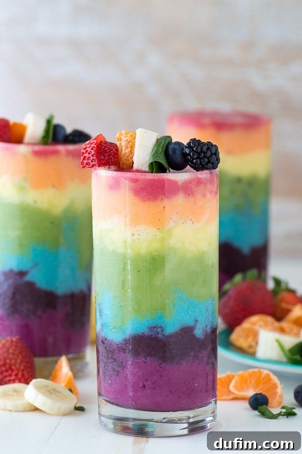 A colorful Rainbow Smoothie in a drinking glass, artfully garnished with fresh blueberries, raspberries, oranges, and strawberries.