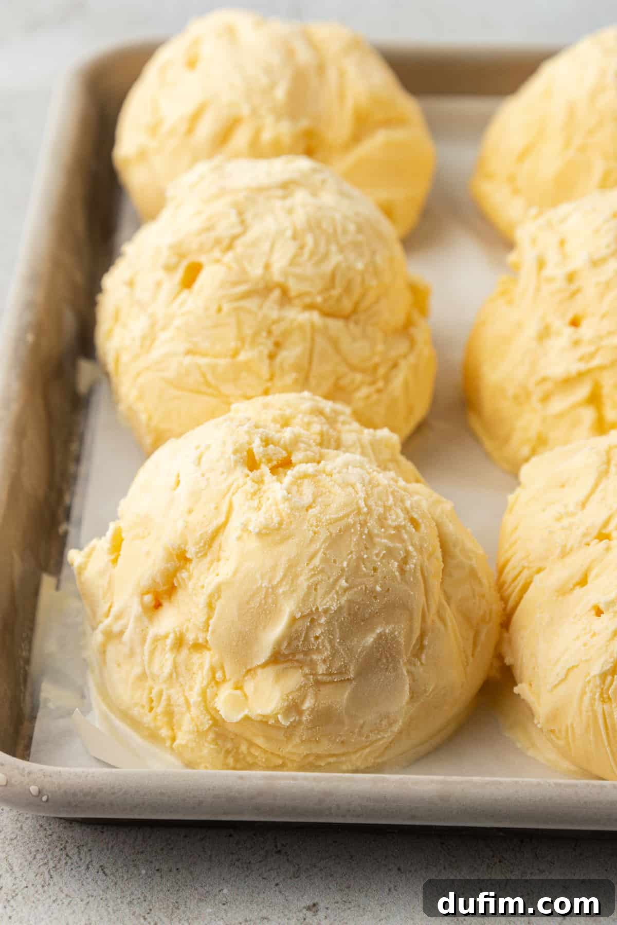 Neatly arranged balls of vanilla ice cream lined up in rows on a sheet pan, perfectly frozen and ready for coating.
