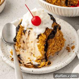 A delectable no-fry fried ice cream on a white plate with a spoon, generously topped with a cherry and whipped cream, ready to be enjoyed.