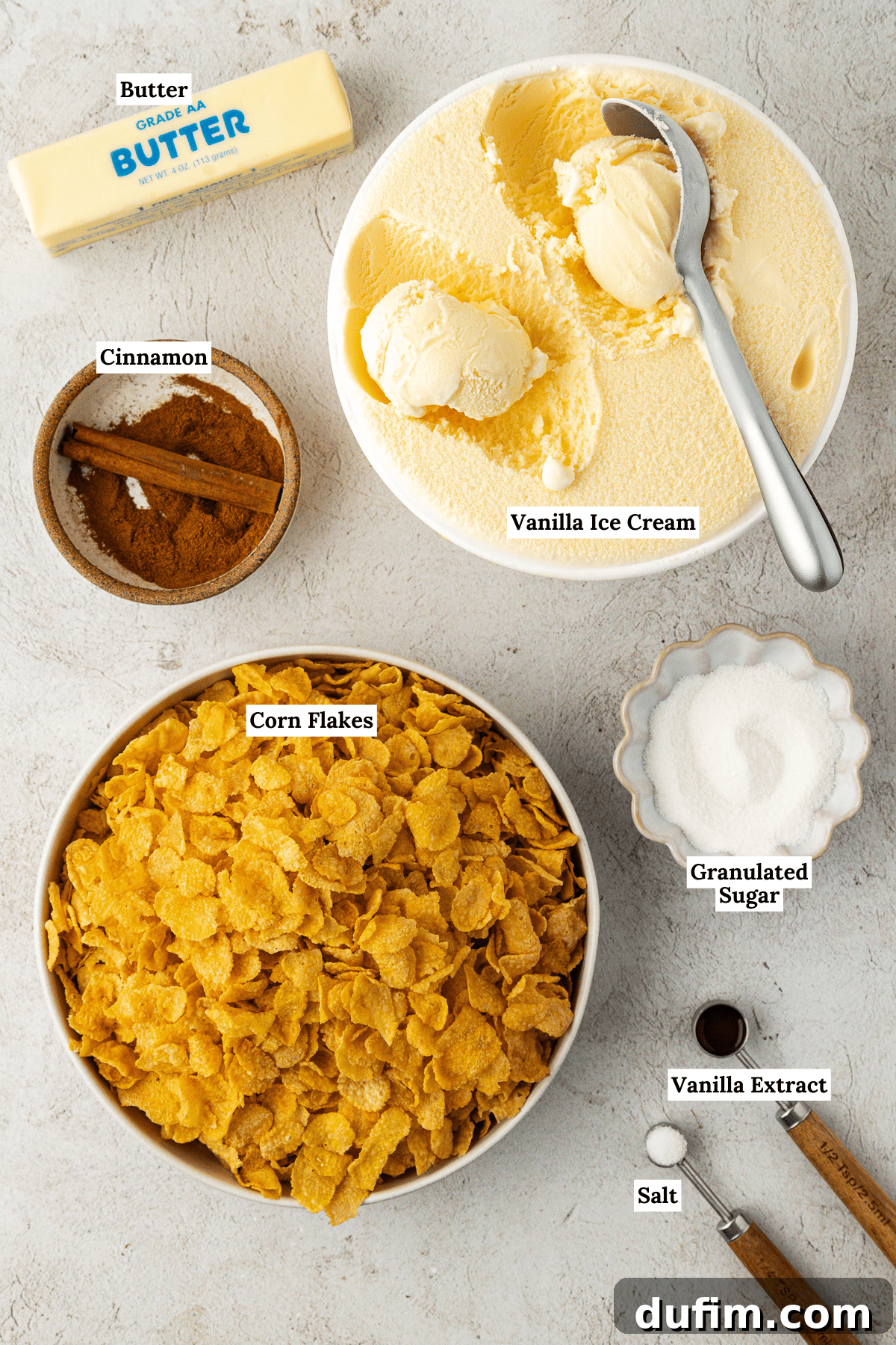 An overhead view showcasing all the essential ingredients for homemade fried ice cream, meticulously arranged. Key components include a container of creamy vanilla ice cream, a stick of butter, a bowl of ground cinnamon, a bag of corn flakes cereal, a pile of granulated sugar, a bottle of vanilla extract, and a pinch of salt.