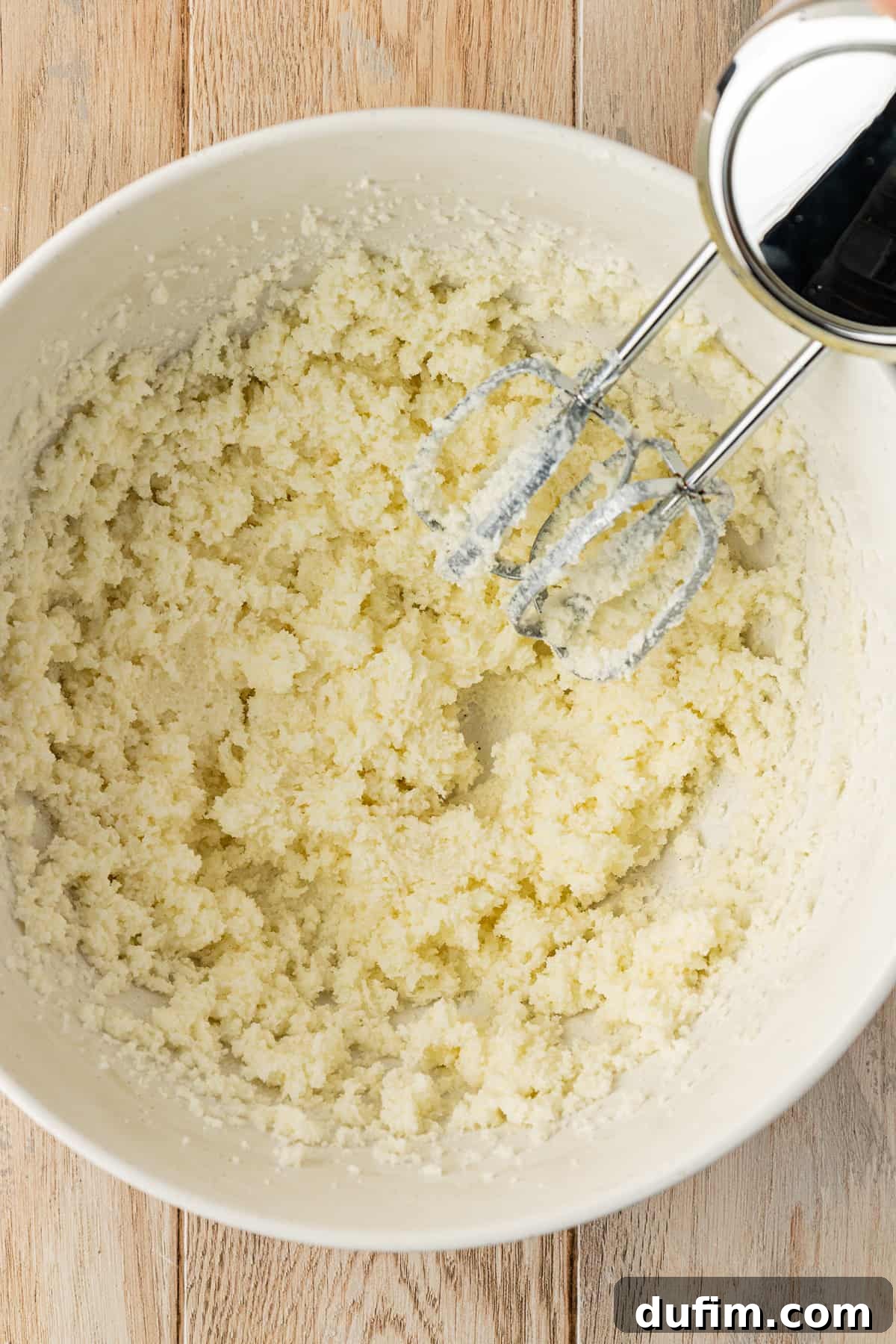 A white bowl on a wood surface with butter and sugar that has been mixed together by an electric mixer, showing the fluffy texture achieved through creaming