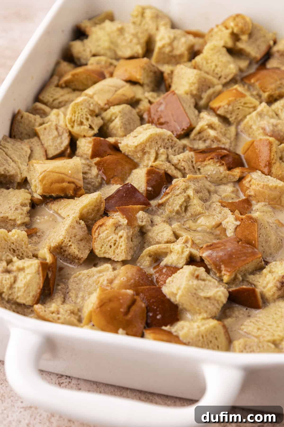 bread cubes soaked in a liquid mixture in a white baking dish