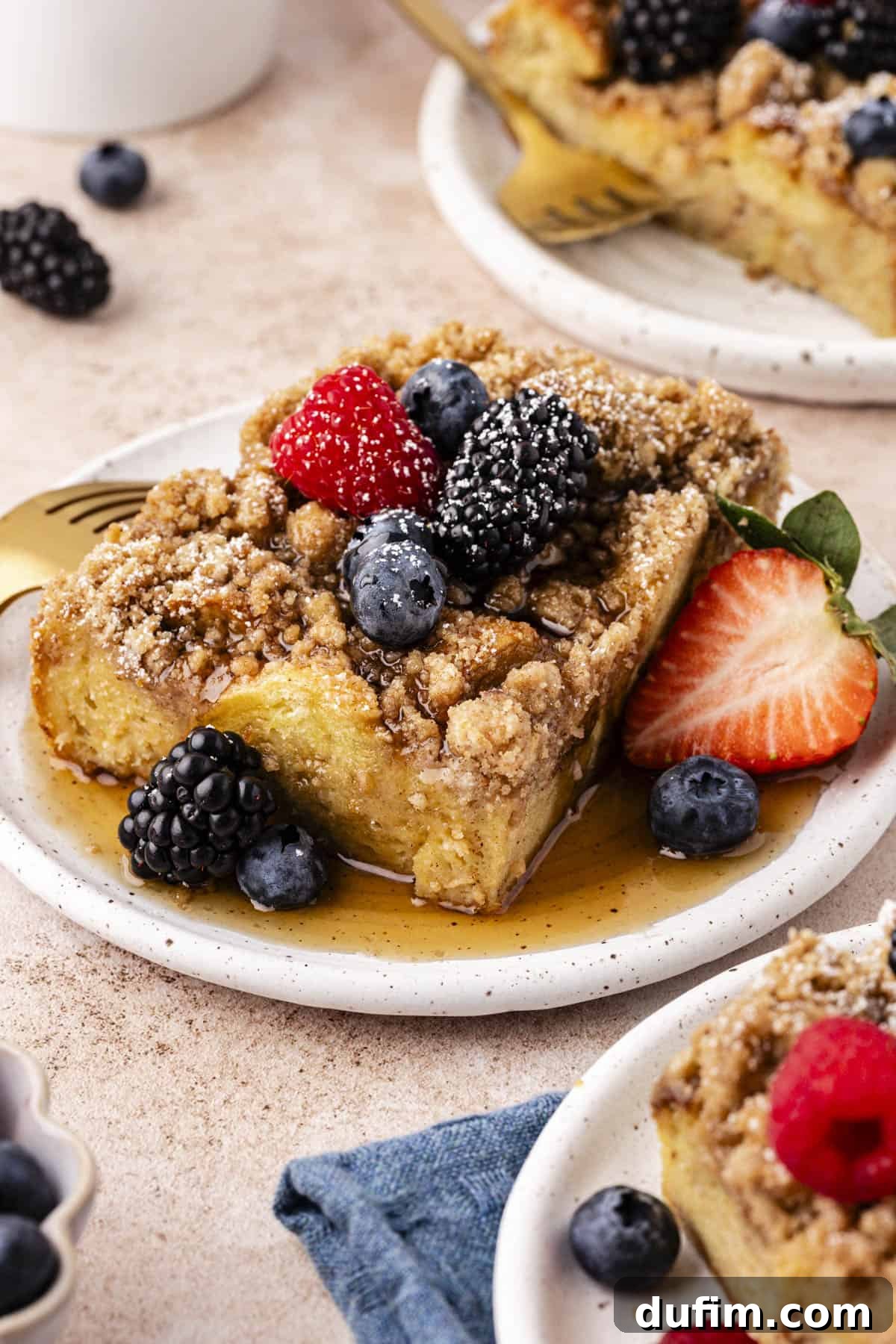 three small plates with slices of french toast casserole on them topped with maple syrup, fresh berries, and a light dusting of powdered sugar