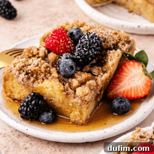 a slice of french toast casserole on a small plate with maple syrup and fresh berries
