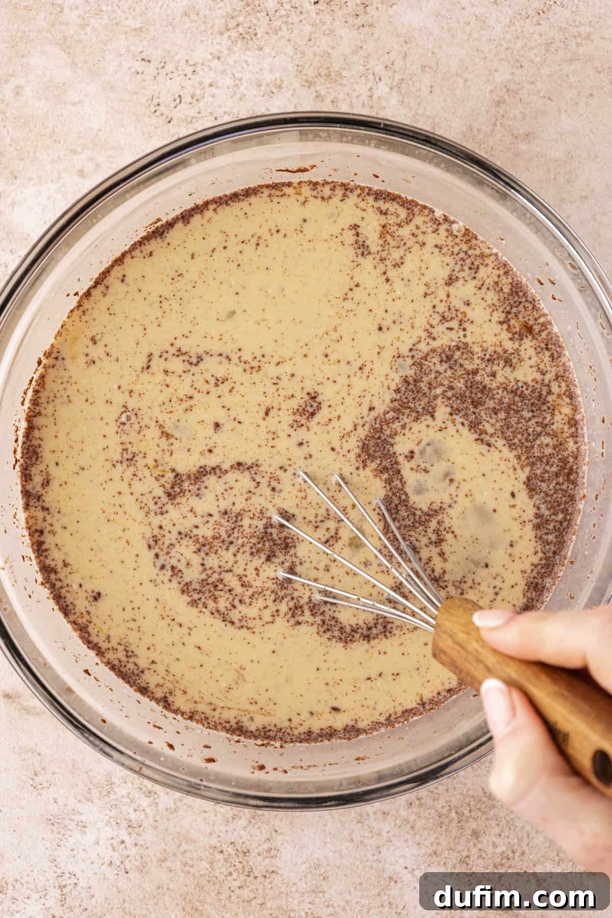 egg custard mixture for french toast being mixed with a wire whisk in a clear glass bowl