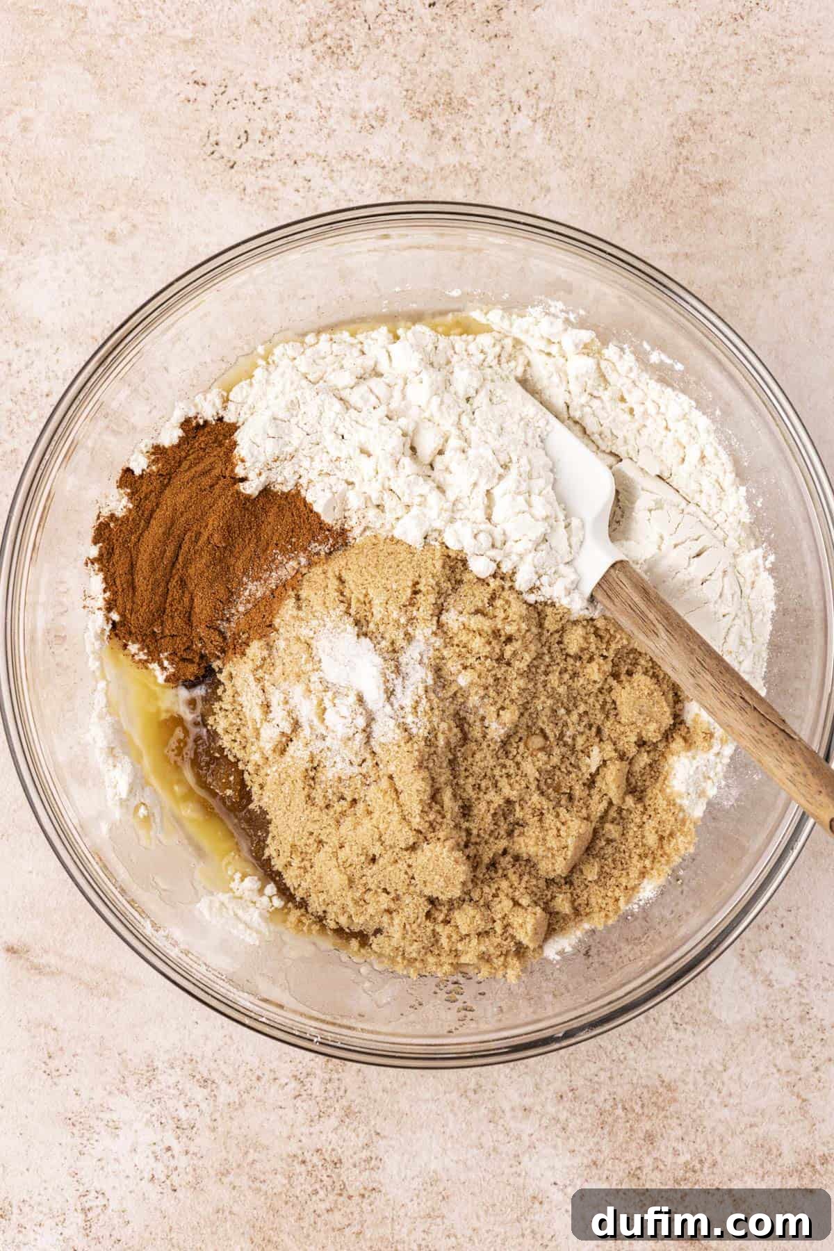 ingredients for french toast casserole in a clear glass bowl with a flour mixture, cinnamon and brown sugar sitting on top, not mixed together yet