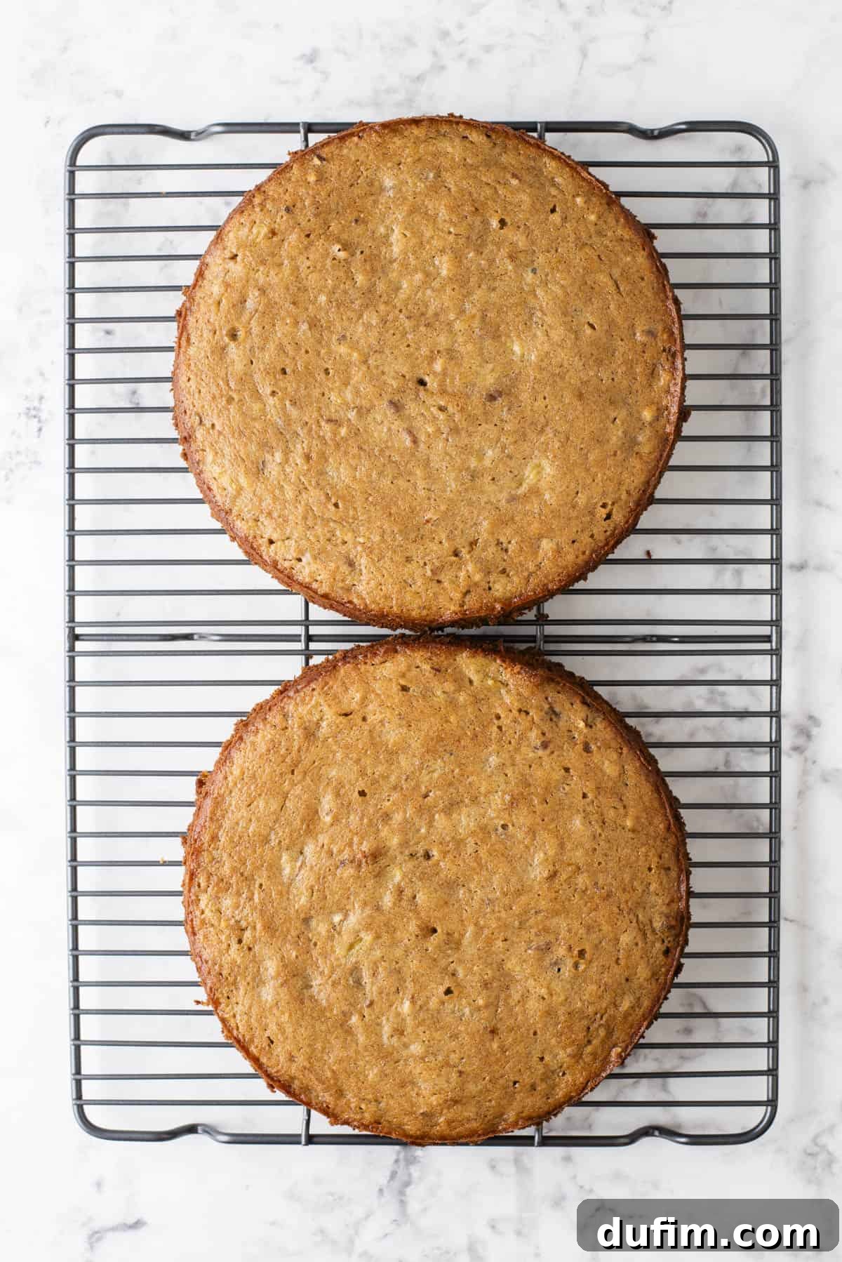 Two freshly baked round hummingbird cakes cooling on a wire rack, displaying their golden-brown tops and moist appearance after baking.
