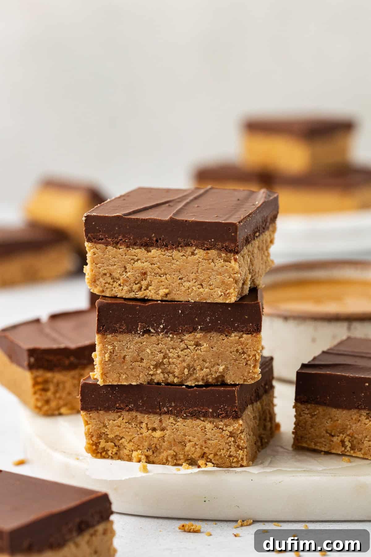 A stack of three peanut butter bars with more bars scattered all around and in the background, highlighting the distinct layers.